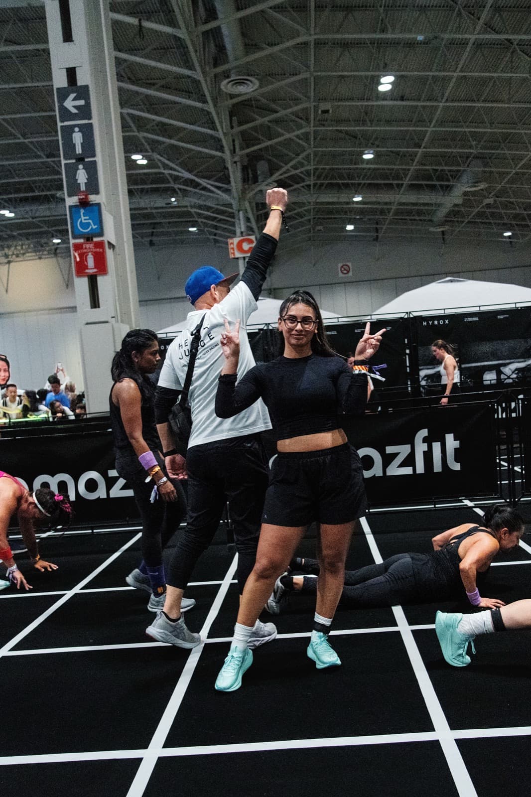 An athlete throwing peace signs on the burpee lane as a judge raises a fist behind her