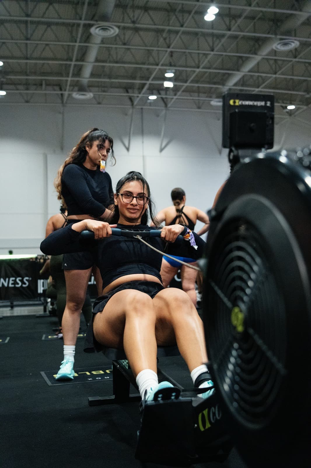 A smiling athlete at the catch on the rower while her partner coaches from behind
