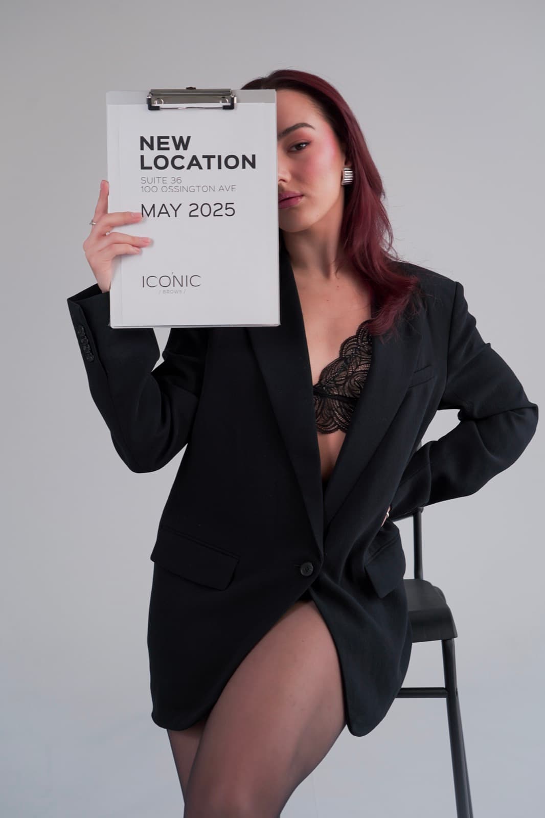 A model in a black blazer covering half her face with a New Location clipboard